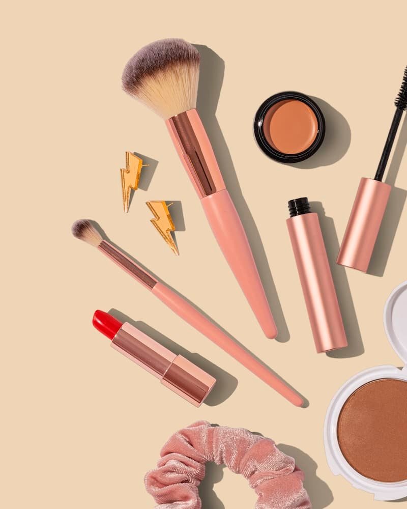 Makeup brushes, lipstick and blush on a warm peach background